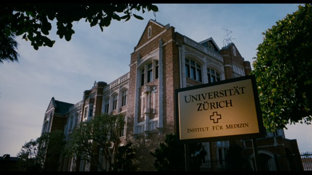 A still from a movie featuring a man standing on a boardwalk in front of an arcade with signs for Skeeball, saltwater taffy, and various attractions.