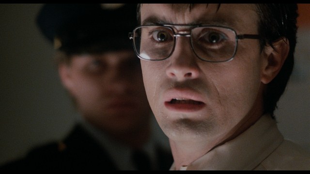 Statue of a smiling figure resembling Jesus, giving a thumbs up gesture, set against a colorful backdrop with signs related to Catholicism.