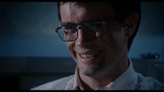 A serious-looking cardinal with a red hat and black robes sitting in a wooden chair in an office, surrounded by colorful posters and memorabilia.