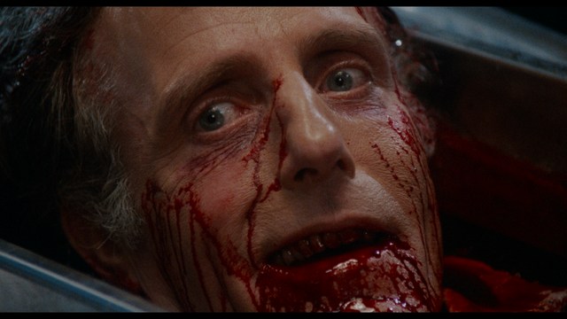 A tense scene featuring a woman with long hair and a serious expression, looking off to the side, while a man with short hair sits in the background, appearing relaxed and slightly turned away.