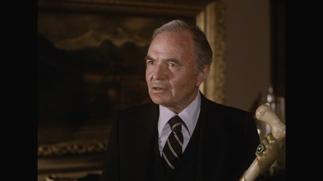 A still image from a film featuring a somber-looking man with dark hair, wearing a hoodie, expressing a concerned or troubled emotion.