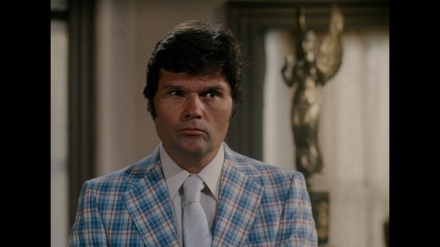 A close-up of a worried man with dark, tousled hair, looking distressed in low-light surroundings.