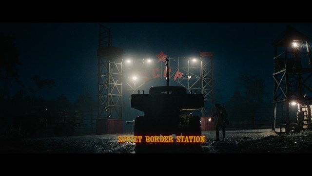 A still from a movie featuring a man standing on a boardwalk in front of an arcade with signs for Skeeball, saltwater taffy, and various attractions.