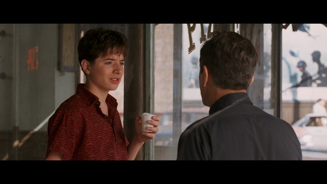 Statue of a smiling figure resembling Jesus, giving a thumbs up gesture, set against a colorful backdrop with signs related to Catholicism.