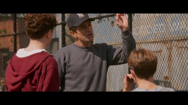 Three young individuals sitting together, two holding hockey sticks, with a casual and intense expression in a domestic setting.
