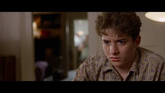 A close-up shot of a man with a distressed expression, featuring dark hair and wearing a blue hoodie, against a softly lit background.