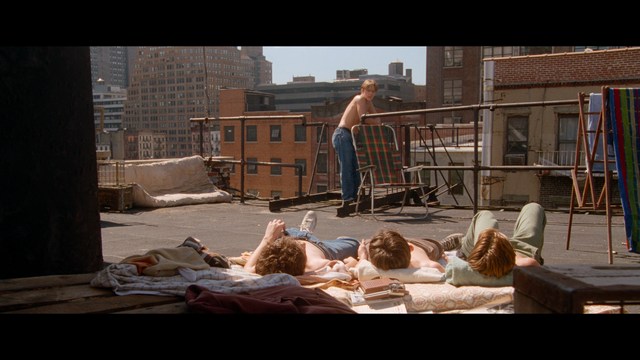 A scene from a movie featuring three characters standing on a bridge with a lush green landscape in the background.