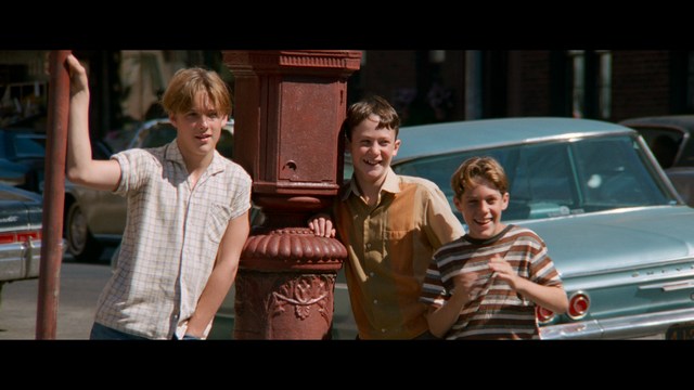 A scene featuring a man with short hair and a beard, wearing a brown jacket and purple shirt, standing outside a restaurant with bright yellow walls and a cartoon cow logo.