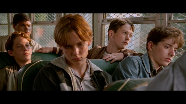 A man with short hair and a beard sits at a table, looking surprised or excited while holding a bottle.