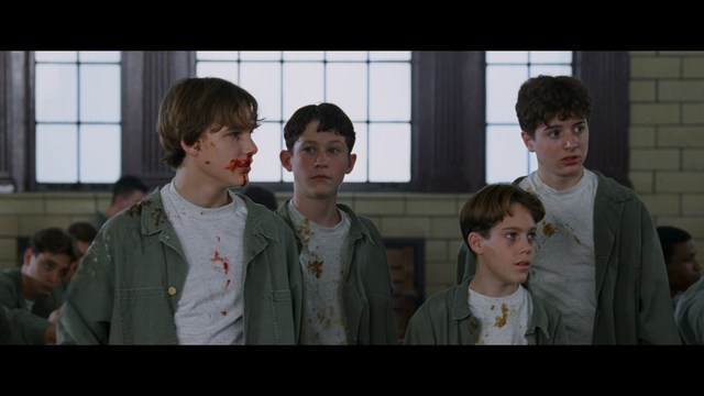 A close-up shot of a man wearing a white suit and a white hat, looking intently at someone in a retail store filled with merchandise.