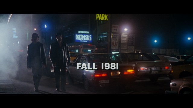 A tense scene featuring a woman with long hair and a serious expression, looking off to the side, while a man with short hair sits in the background, appearing relaxed and slightly turned away.