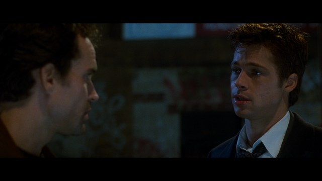 A scene from the film showing two male characters, one in a futuristic helmet and uniform, smiling while the other appears tense, conveying a sense of intrigue.