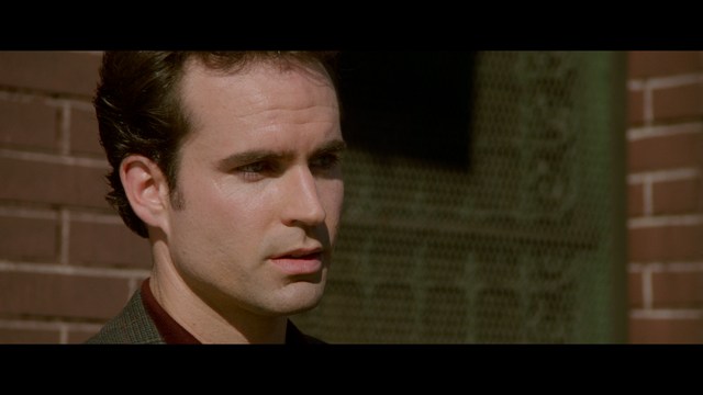 A close-up of an elderly man with a beard and white attire, appearing serious and contemplative, set against a colorful, futuristic background.