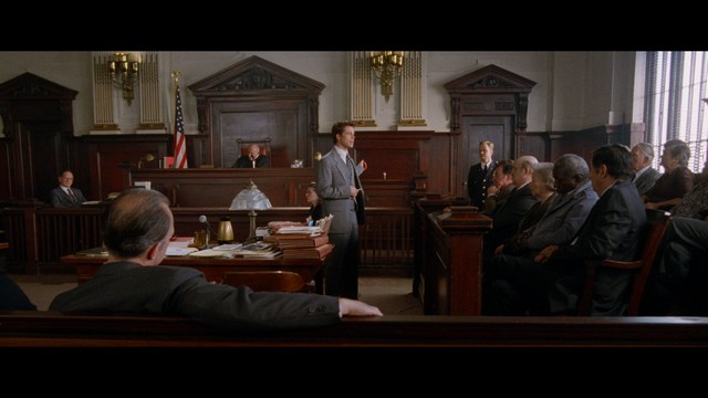 A close-up of an elderly man with a beard and white attire, appearing serious and contemplative, set against a colorful, futuristic background.