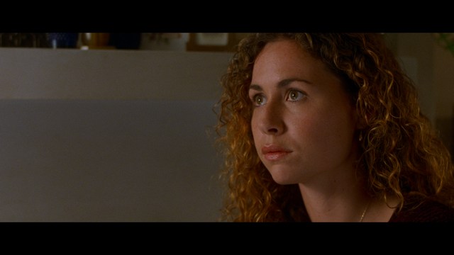 A close-up of an elderly man with a beard and white attire, appearing serious and contemplative, set against a colorful, futuristic background.