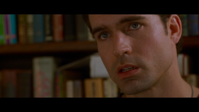 A close-up of an elderly man with a beard and white attire, appearing serious and contemplative, set against a colorful, futuristic background.