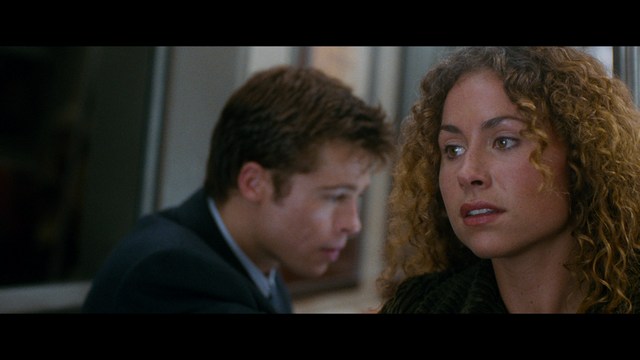 A close-up of an elderly man with a beard and white attire, appearing serious and contemplative, set against a colorful, futuristic background.
