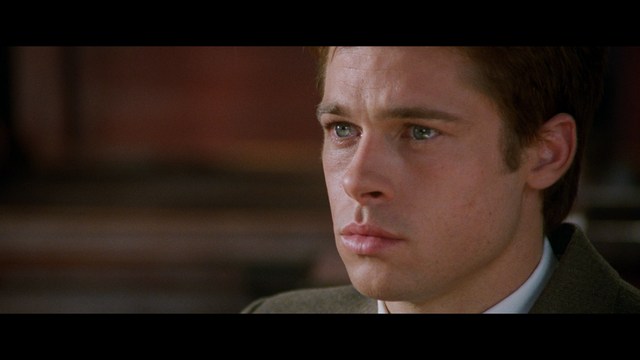 A close-up of an elderly man with a beard and white attire, appearing serious and contemplative, set against a colorful, futuristic background.