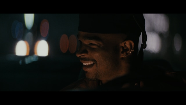 Two young men are looking at something off-camera, standing inside a building with bright lighting and seating areas visible in the background.