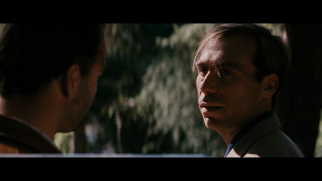 A scene from the film showing two male characters, one in a futuristic helmet and uniform, smiling while the other appears tense, conveying a sense of intrigue.