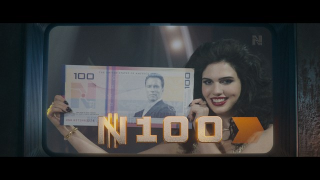 A serious-looking cardinal stands in front of a wooden backdrop with colorful posters related to Catholicism, holding a microphone at a press conference.