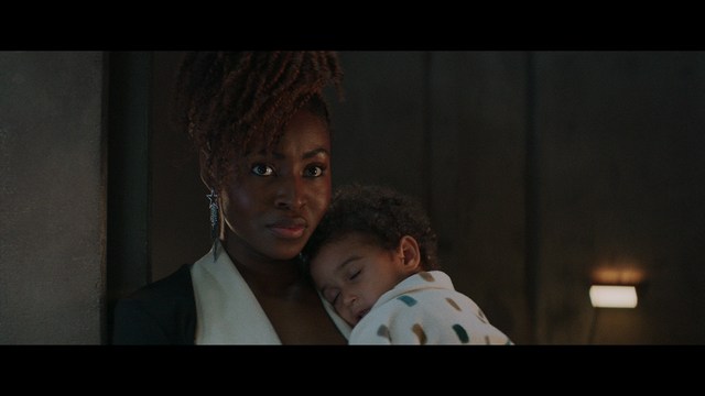 A scene from a movie featuring two young men sitting closely together in an airport waiting area, with one holding a box of popcorn.