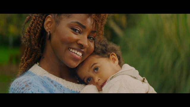 A woman with dark hair and a neutral expression sitting in a retro diner setting.