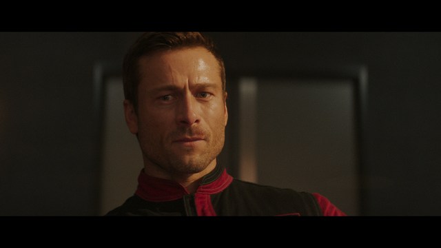 A young man pointing a handgun while seated in a bus, showcasing an intense expression.