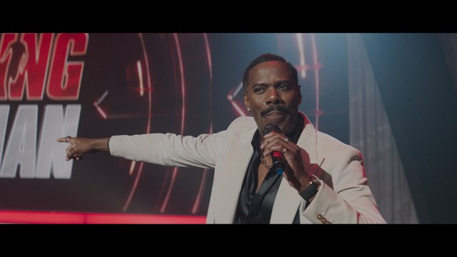 A golden trophy statue of a goblin-like character positioned on a wooden table in an office setting, with large windows and a building facade visible in the background.