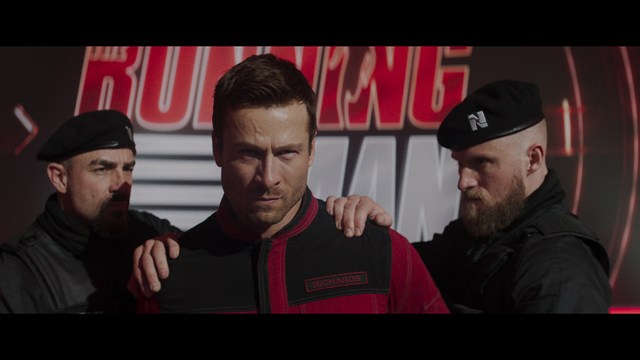 A man with short hair and a beard sits at a table, looking surprised or excited while holding a bottle.