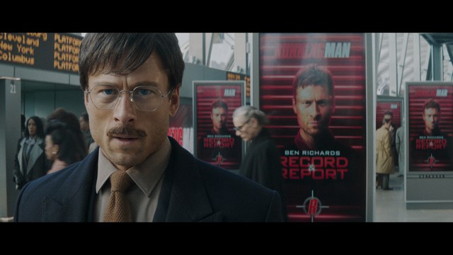 A woman seated at a restaurant table, thoughtfully resting her chin on her hand while reading a newspaper. Blurred figures of two people can be seen in the background.