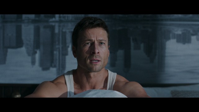 A man with dark, styled hair and a subtle smile seated at a restaurant table, with blurred diners in the background.