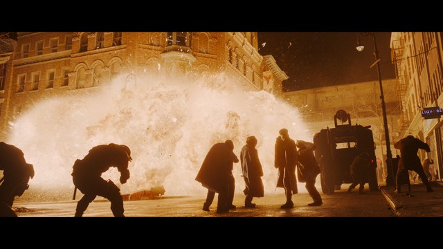 A serious-looking cardinal with a red hat and black robes sitting in a wooden chair in an office, surrounded by colorful posters and memorabilia.