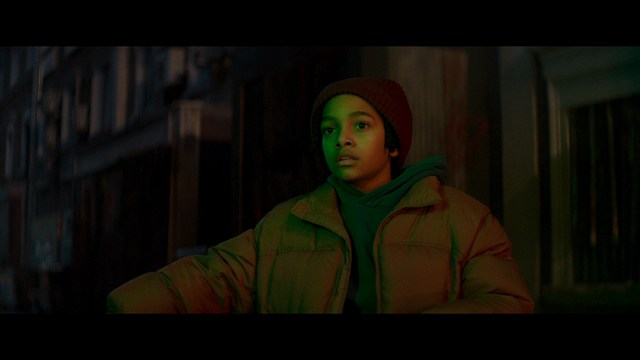 Two figures walking on a road towards a blue 'Welcome to New Jersey' sign.