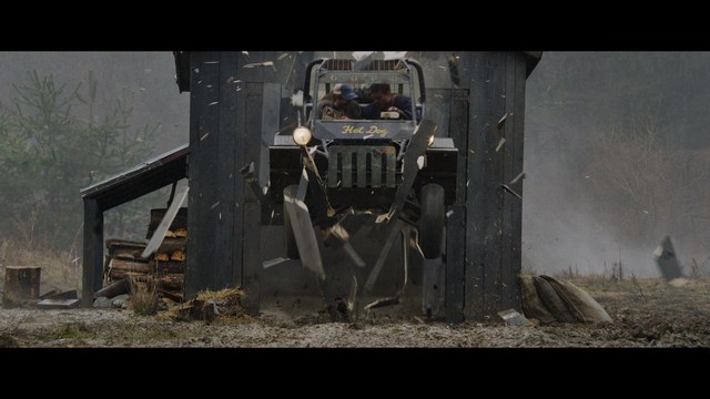 A scene from a film featuring two characters, one elderly woman holding a small object and speaking animatedly, and a young man listening intently, surrounded by lush greenery and plants in a greenhouse setting.