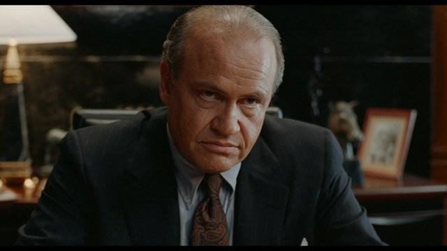 A scene from a movie featuring two young men sitting closely together in an airport waiting area, with one holding a box of popcorn.