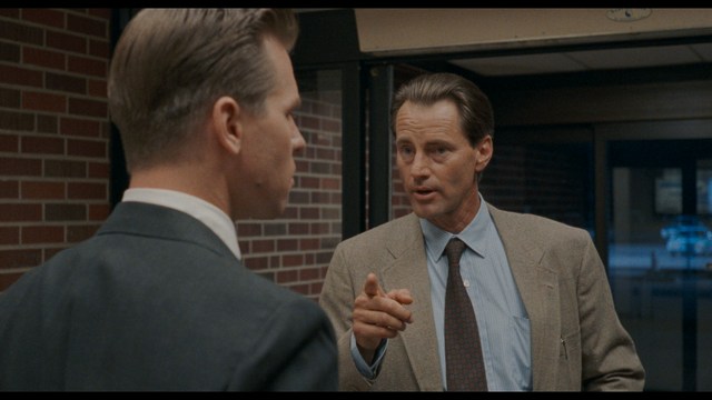 A group of people standing in a church, with a focus on a woman in a striped blazer looking up, while others are holding books or looking ahead.