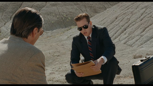 Four anthropomorphic turtles in ninja attire stand in a dimly lit room, while a humanoid character with fur sits nearby.