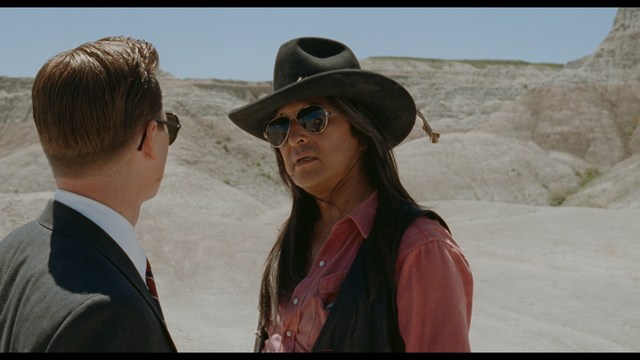 Three young individuals sitting together, two holding hockey sticks, with a casual and intense expression in a domestic setting.