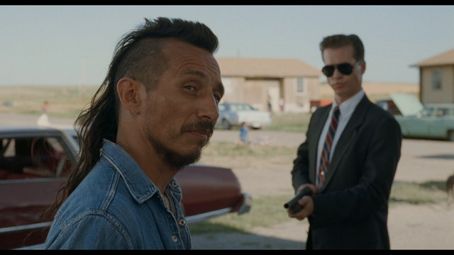 A woman with dark hair and a neutral expression sitting in a retro diner setting.