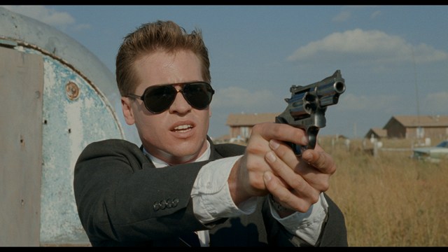 A young man pointing a handgun while seated in a bus, showcasing an intense expression.