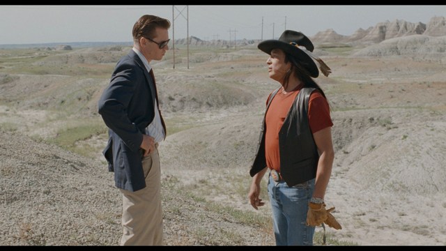 A scene from a movie featuring three characters standing on a bridge with a lush green landscape in the background.