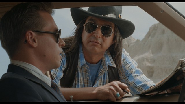 A golden trophy statue of a goblin-like character positioned on a wooden table in an office setting, with large windows and a building facade visible in the background.