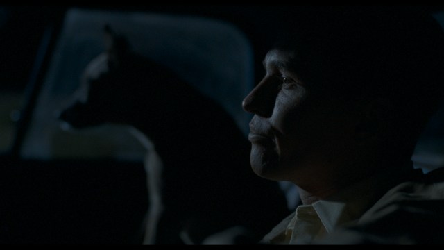 A serious-looking cardinal with a red hat and black robes sitting in a wooden chair in an office, surrounded by colorful posters and memorabilia.
