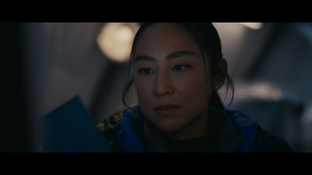A man in a white suit and hat stands at a doorway, smiling, with a suburban landscape in the background.