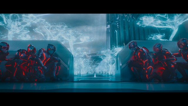 A golden trophy statue of a goblin-like character positioned on a wooden table in an office setting, with large windows and a building facade visible in the background.