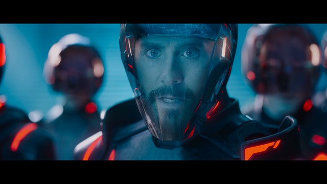 Close-up of a woman with long black hair sitting in a restaurant, looking concerned. A colorful painting is visible in the background, along with red bar stools.