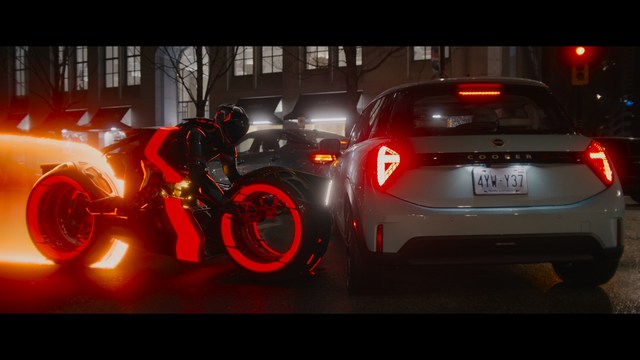 A woman seated at a restaurant table, thoughtfully resting her chin on her hand while reading a newspaper. Blurred figures of two people can be seen in the background.