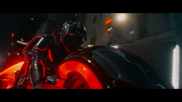 A man with dark, styled hair and a subtle smile seated at a restaurant table, with blurred diners in the background.
