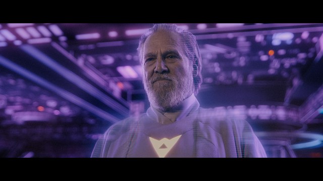A scene from a film featuring two characters, one elderly woman holding a small object and speaking animatedly, and a young man listening intently, surrounded by lush greenery and plants in a greenhouse setting.